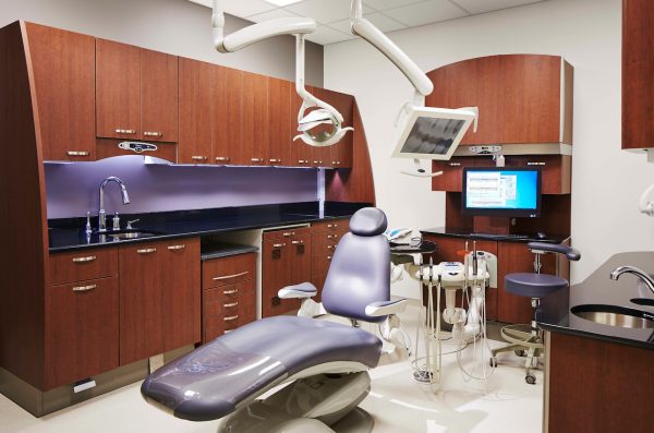 a dentist's room with a dental unit and tools and brown cabinets