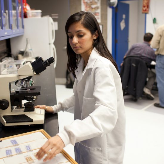 UIC science student wearing white coat working with microscope at laboratory