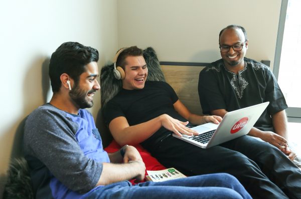 three students sitting holding a laptop with UIC sticker and laughing