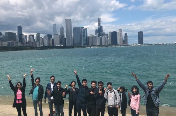 International students pose with hands held high by the shore of Lake Michigan with the Chicago skyline in the background.