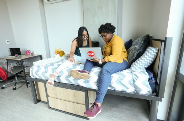 two UIC students sitting on a bed looking at a laptop