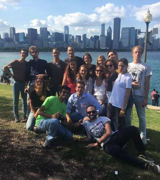 A group of international students pose along the shore of Lake Michigan with the Chicago skyline behind them on a sunny, summer day.