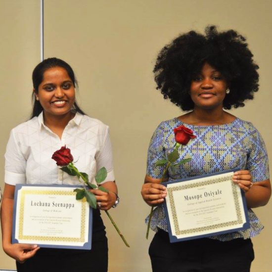 two international students posing holding roses and their certificates