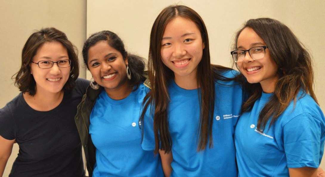 Four students link arms and smile at the camera. Three are wearing blue First Friends t-shirts.