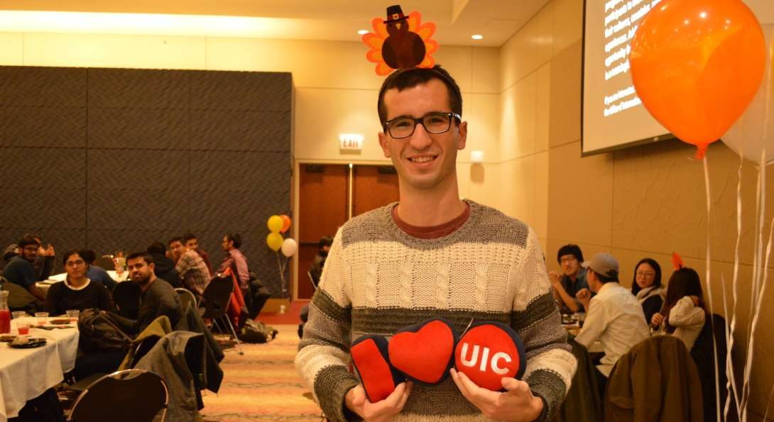 student holding I love UIC stuffed toys and smiling with people sitting at dinner tables in the background