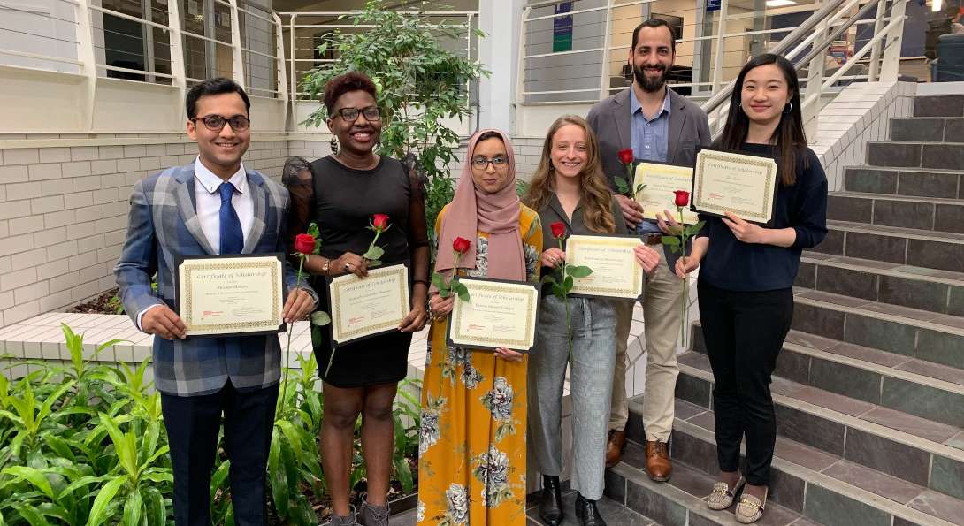 seven people posing with certificates and roses in hand