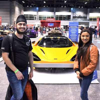 Two students stand in front of a yellow sports car, smiling.