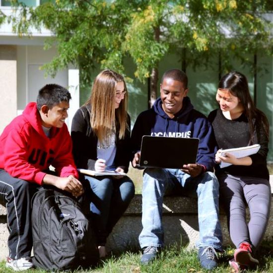 Four students view a laptop outside a UIC campus building.