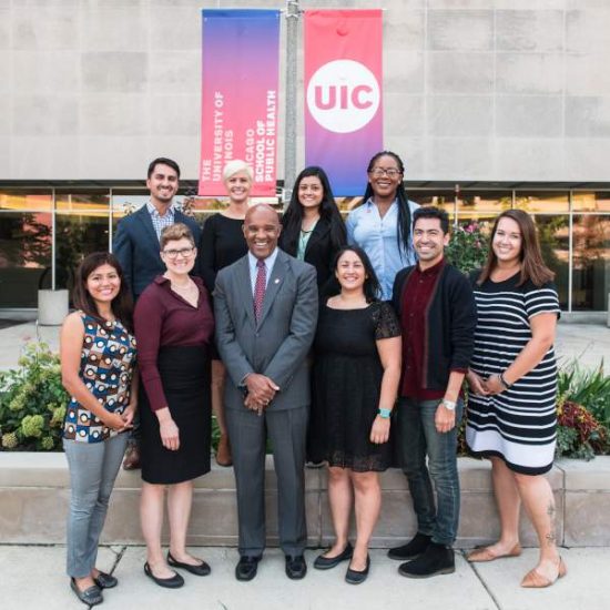 A group of individuals in professional clothing stand and smile in front of UIC banners.
