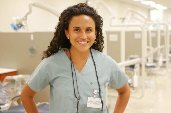 Individual wearing scrubs with hands on hips, smiling at the camera.