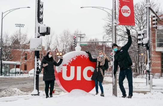 Students stand beside the UIC circle mark covered in snow.