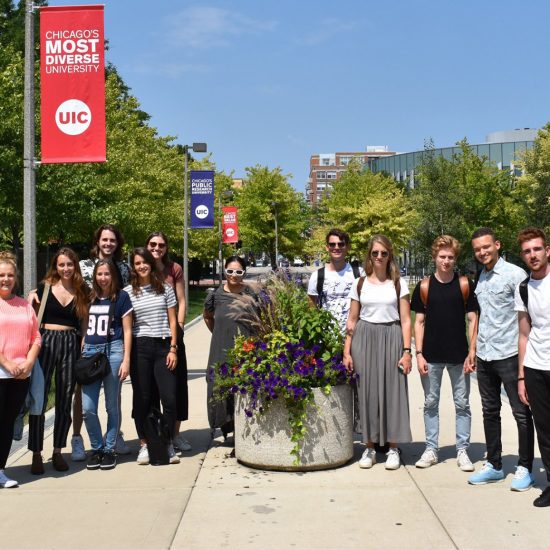 Twelve UIC exchange students carrying bags pose outside campus on a sunny day.