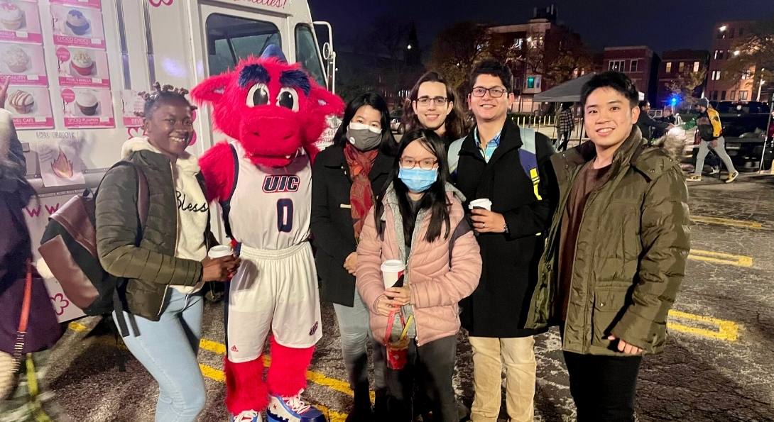 Six UIC students pose with Sparky the Dragon during the 2021 Homecoming Tailgate