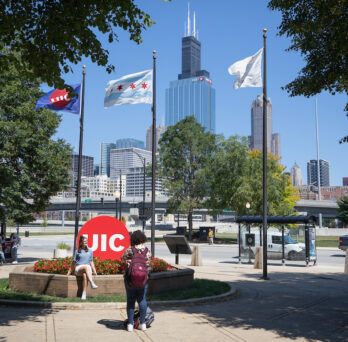 View of the UIC circle mark on east campus with three flags and the Chicago skyline in the background. 