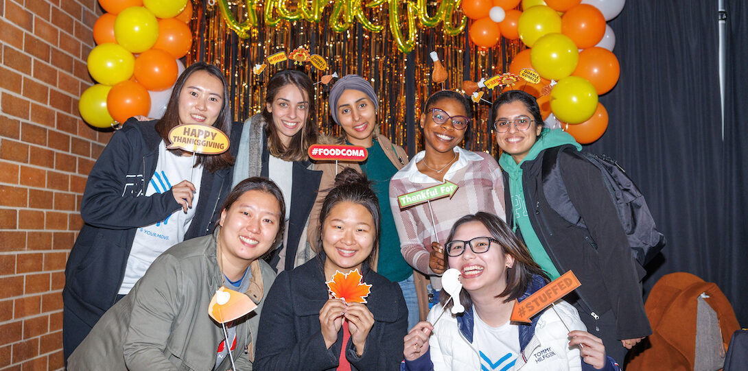 Group of students pose in front of the photo backdrop with Thanksgiving props.