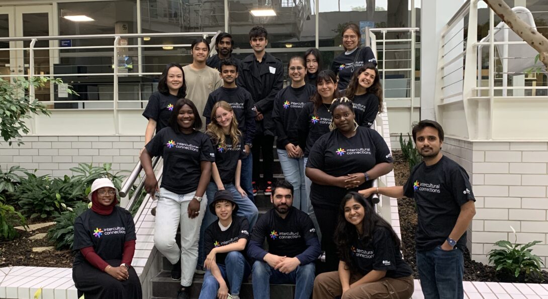 Group of students wearing the Intercultural Connections t-shirt pose on the stairs of the SSB lobby.
