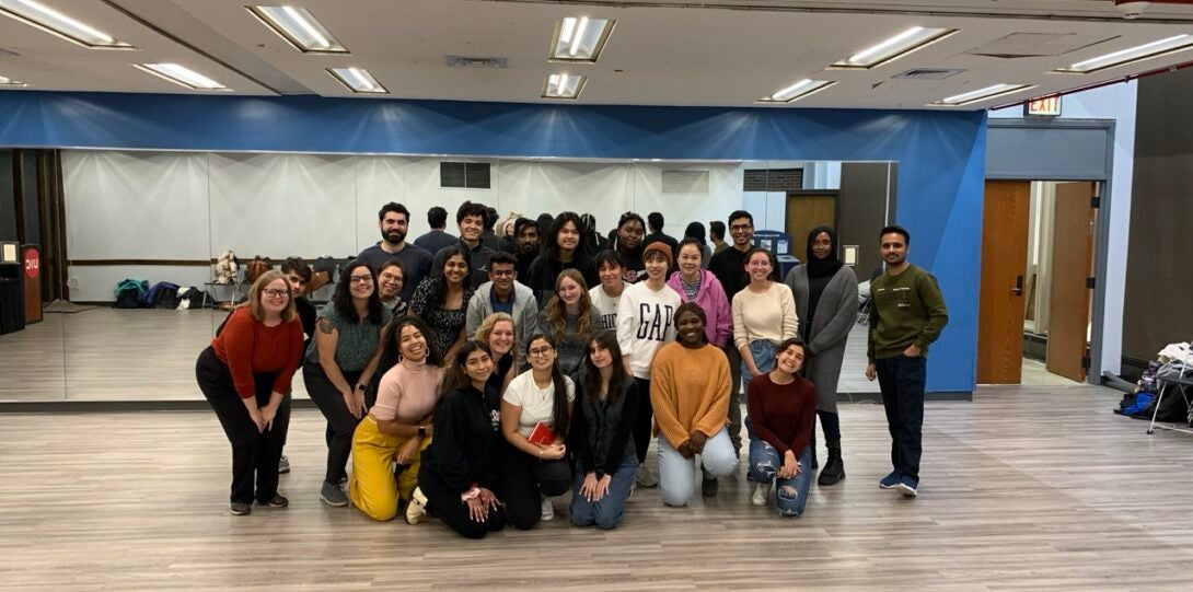 A large group of students pose in front of a mirror at the end of a dance class.