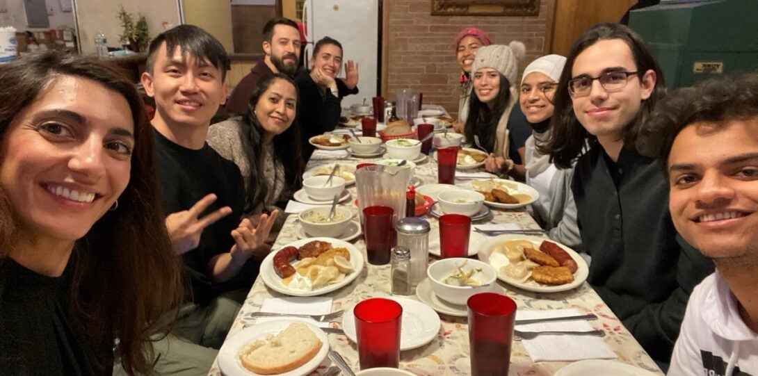 A group of students sit around a table filled with food and drink.