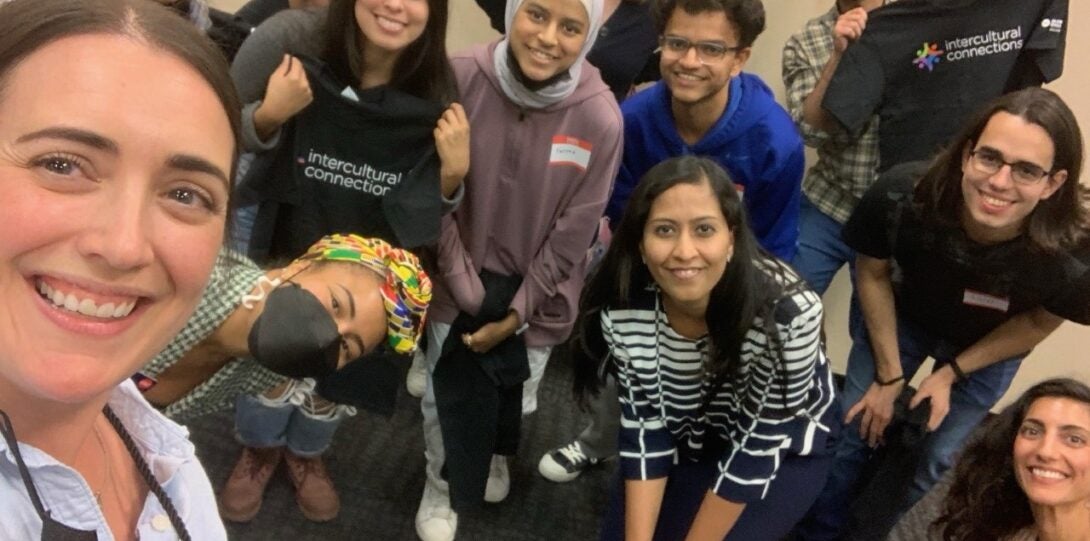 A group of students and staff take a selfie while holding the black Intercultural Connections t-shirts.